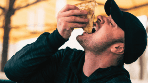 A Man Dressed In Black Eating a Slice Of Pizza 