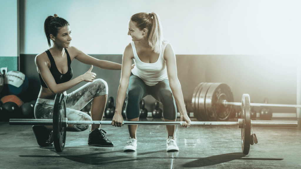 A Woman Doing Dead Lift While Another Woman Is Admiring Her Efforts 