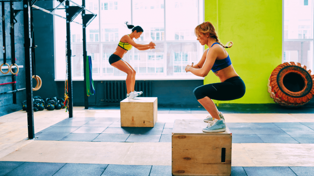 Two Women Doing Box Jumps At The Gym 