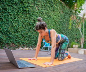 a woman working out outdoor on a yoga mat and laptop 