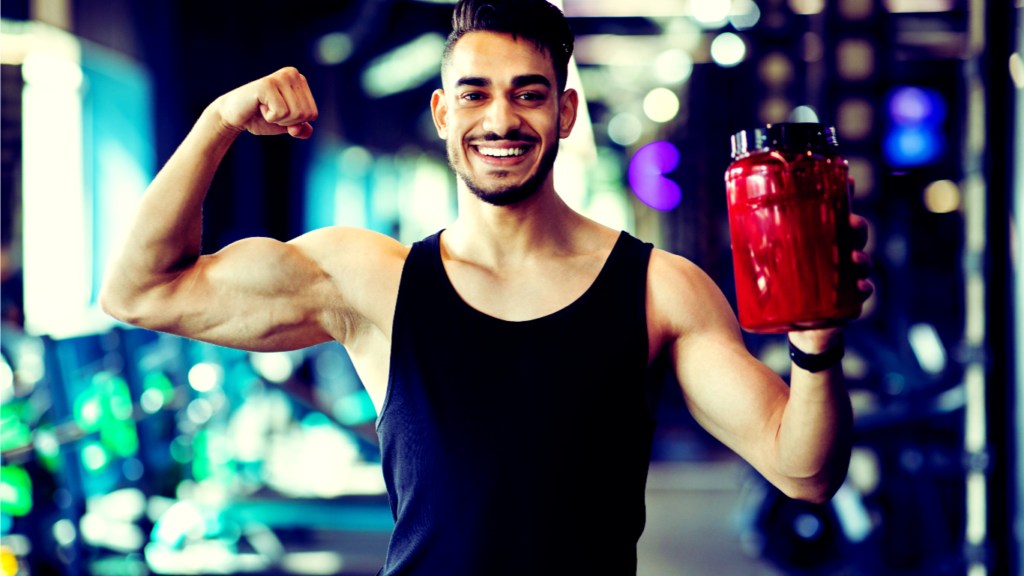 A Man Showing Bicep While Holding Supplement At The Gym 