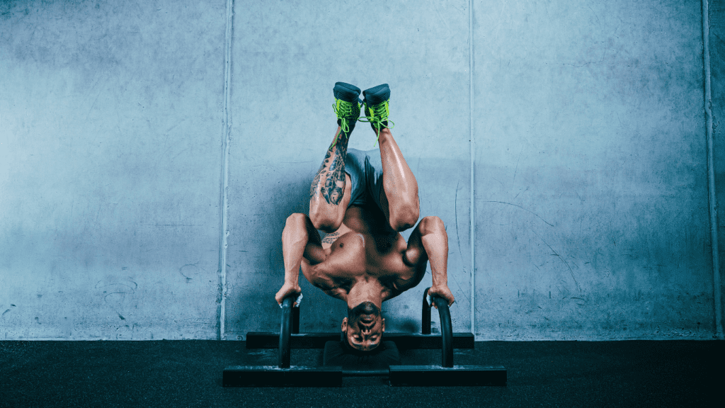 A Strong Muscular Man Doing Handstand Push-Ups On A Wall Using Parallel Bars